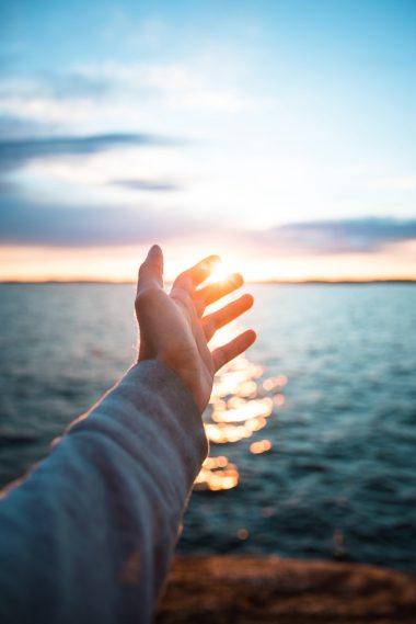 A vertical shot of a hand with the beautiful sea in the background during suns