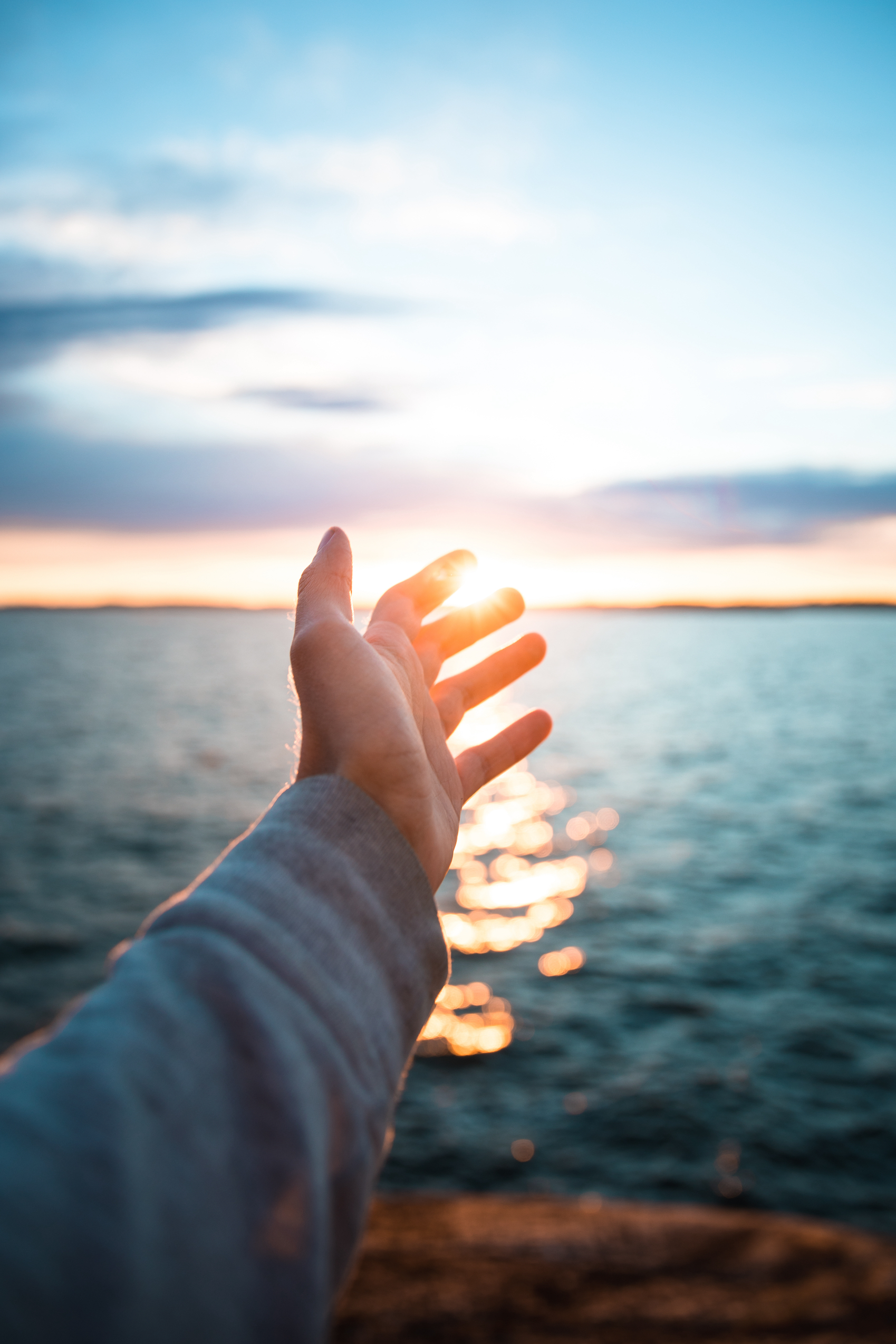 A vertical shot of a hand with the beautiful sea in the background during suns
